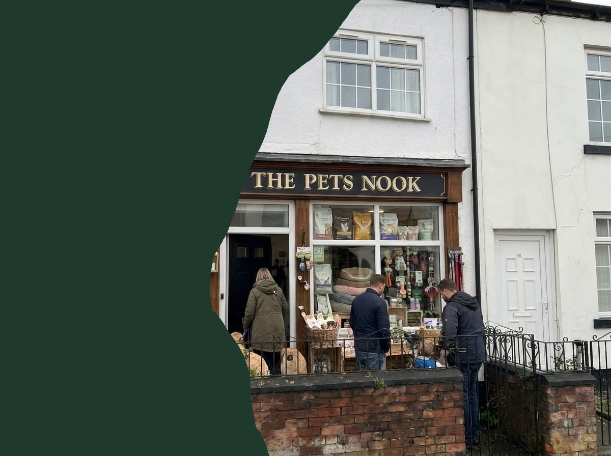 The exterior of a shop named 'THE PETS NOOK' with three people standing in front of the storefront, which is set in a residential street with neighboring houses.